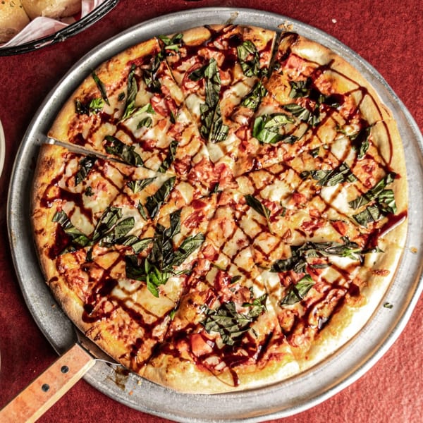 A sliced Pronto's Italian pizza with basil, tomatoes, mozzarella, and balsamic glaze on a metal pan.