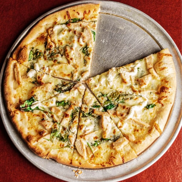 A white pizza with chicken and spinach, one slice removed, on a metal tray.