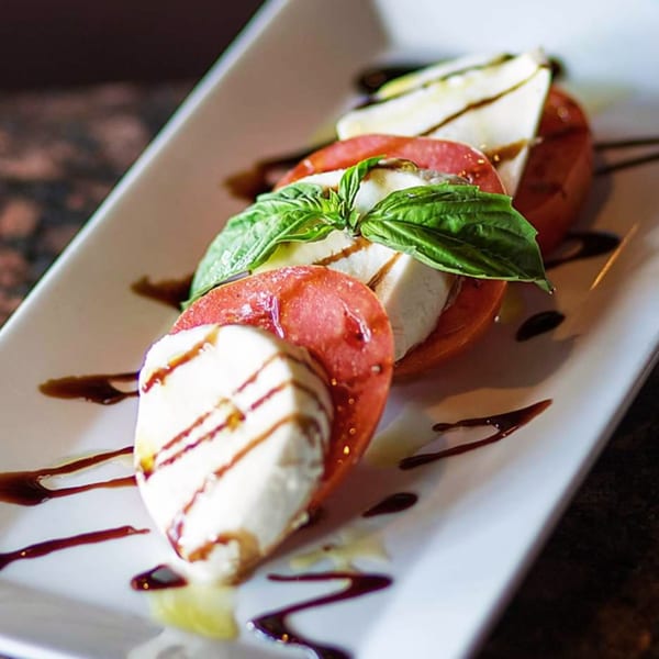 Caprese salad with sliced tomatoes, mozzarella, fresh basil, and balsamic glaze on a white plate.