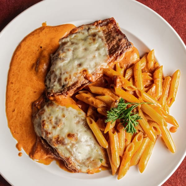 Chicken parmesan with penne pasta in a creamy tomato sauce, garnished with parsley on a white plate.