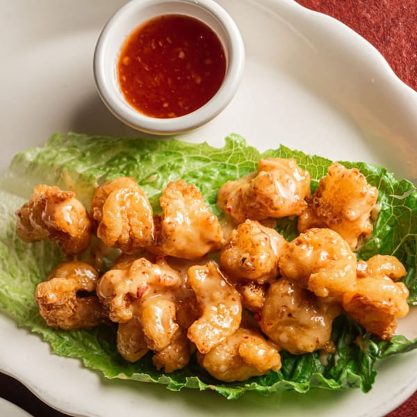 Crispy fried shrimp coated in a creamy sauce, served on lettuce with a side of red dipping sauce.