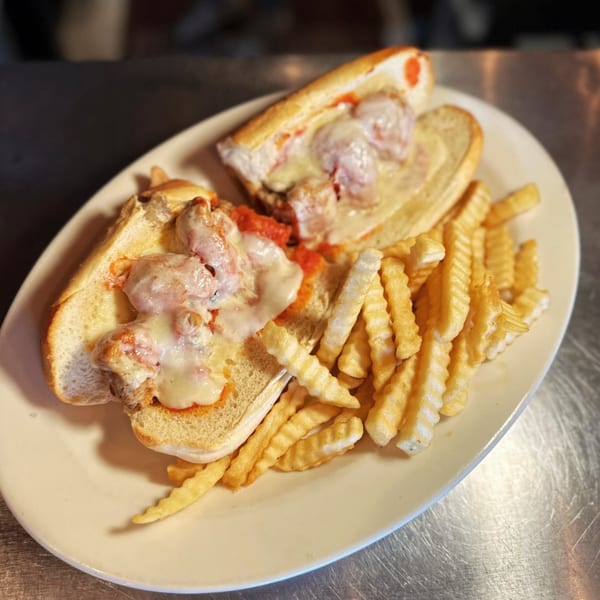 Two meatball subs with melted cheese and tomato sauce, served with crinkle-cut fries on a white plate.