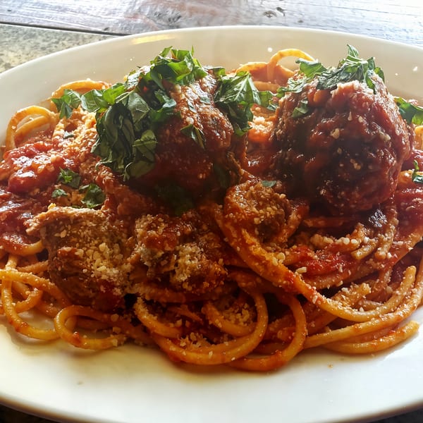 Spaghetti with large meatballs, red sauce, grated cheese, and fresh basil on a white plate.