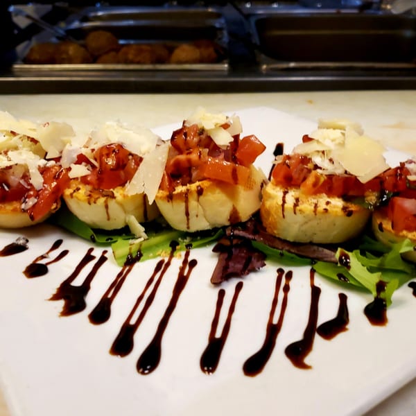 Platter of bruschetta with diced tomatoes, parmesan, and balsamic glaze on a bed of greens.