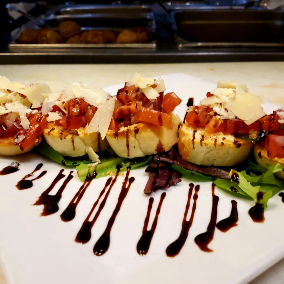 Platter of bruschetta with diced tomatoes, parmesan, and balsamic glaze on a bed of greens.