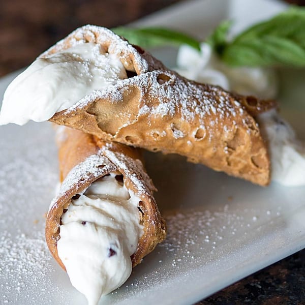 Two cannolis filled with white cream and chocolate chips, dusted with powdered sugar on a white plate.